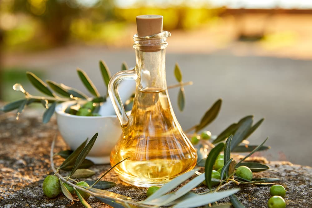 Olive oil bottle next to fresh olives at sunset
